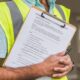 Person in a yellow safety vest holding a pen and a clipboard with an inspection checklist